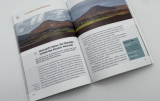 Aufgeschlagener Reiseführer mit doppelseitigem Panorama einer Berglandschaft und redaktionellem Layout auf weißem Hintergrund.